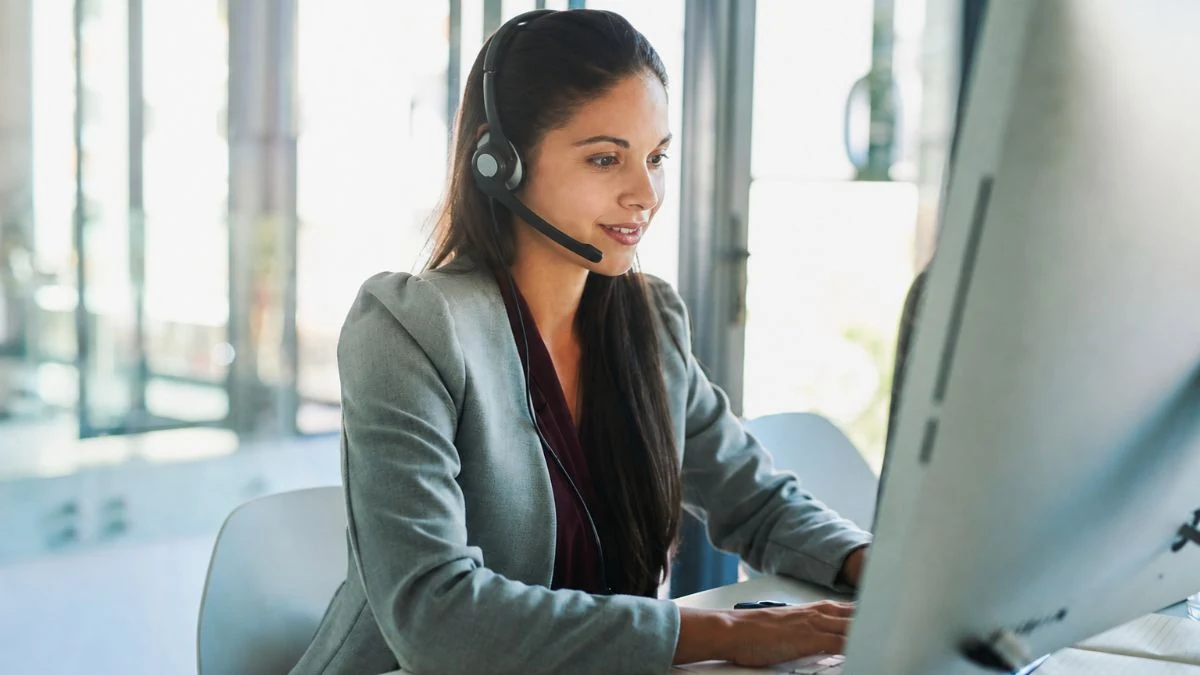 Insurance agent wearing a headset, smiling while typing at a desktop computer