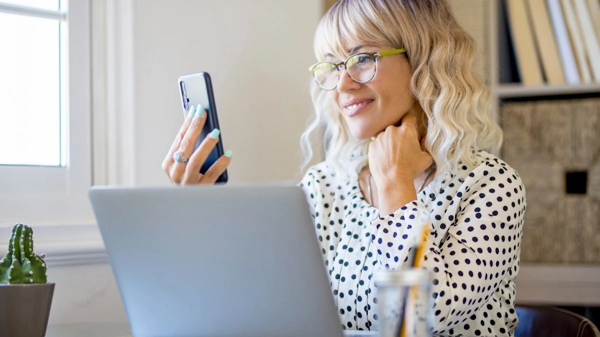 Sales rep smiling at her phone while practicing a call at a laptop