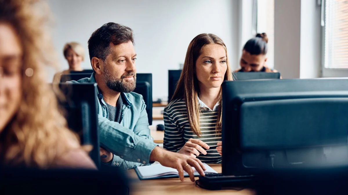 Experienced rep pointing at a screen while coaching a new colleague at the next desk