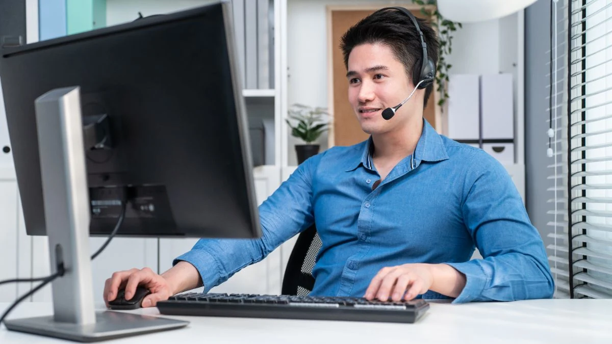 New account executive in a blue shirt on a headset call at his desk