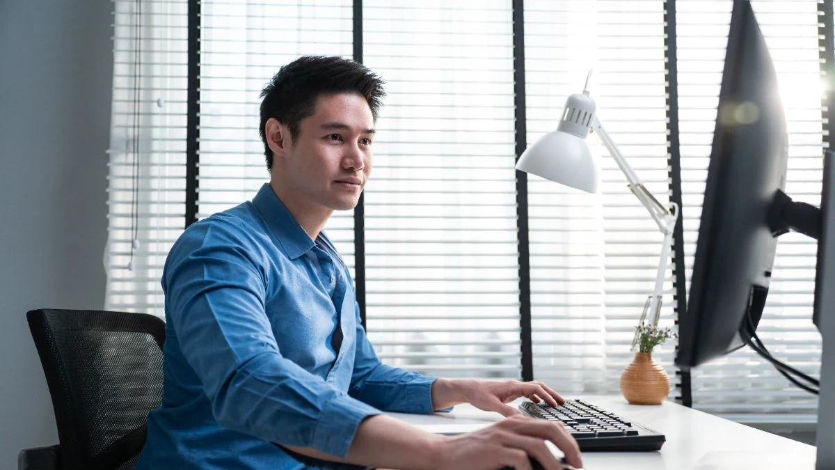 Sales rep in a blue shirt working at his monitor by a window
