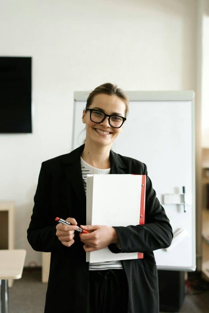 Professional woman in a classroom holding documents and smiling warmly.