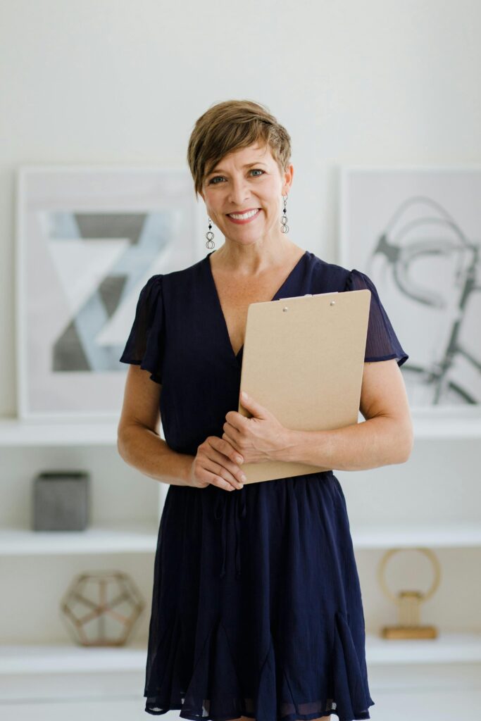 Woman with short hair holding a clipboard in a minimalist indoor setting.